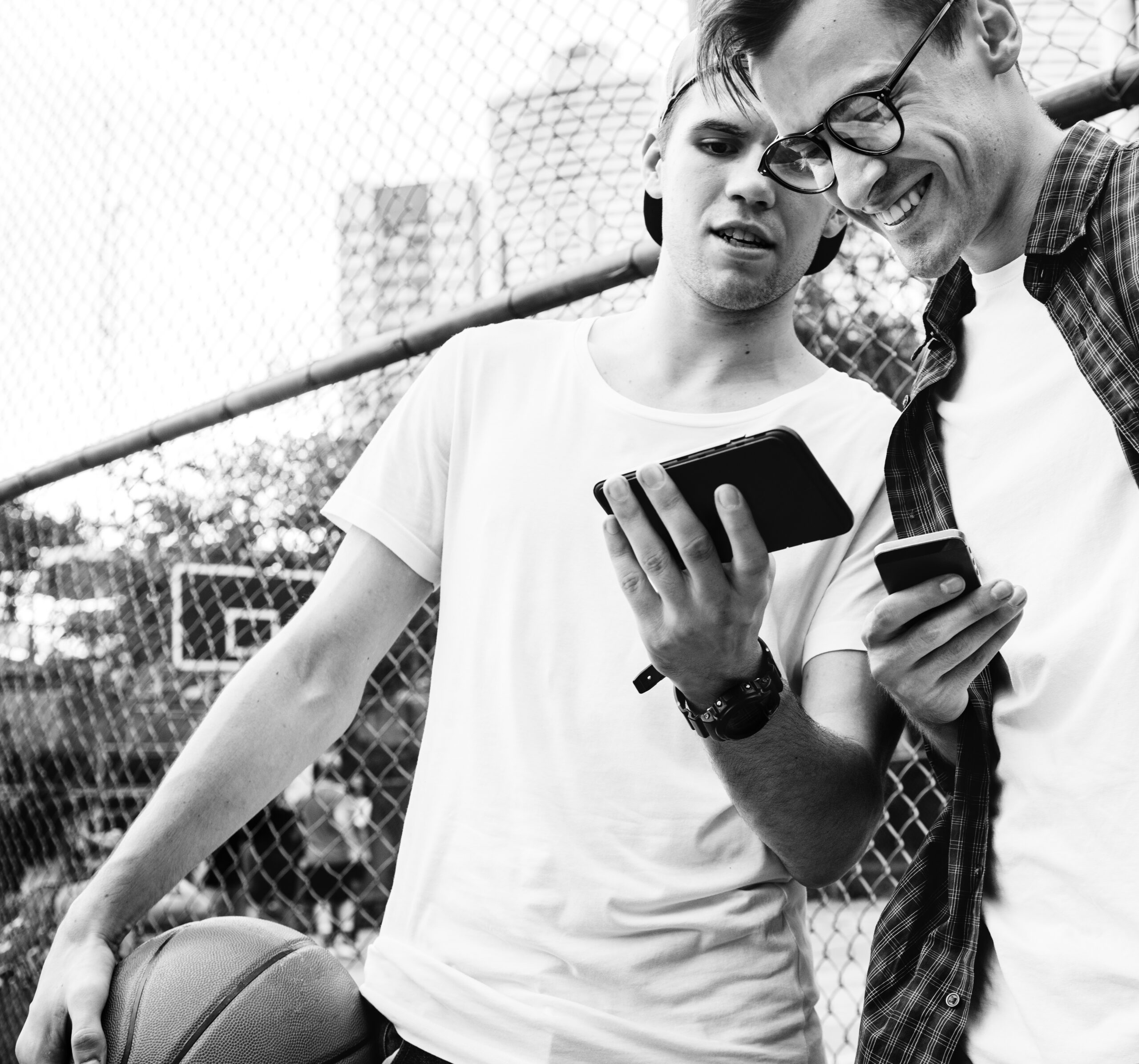 Young adult male friends on the basketball court using smartphones millennials concept